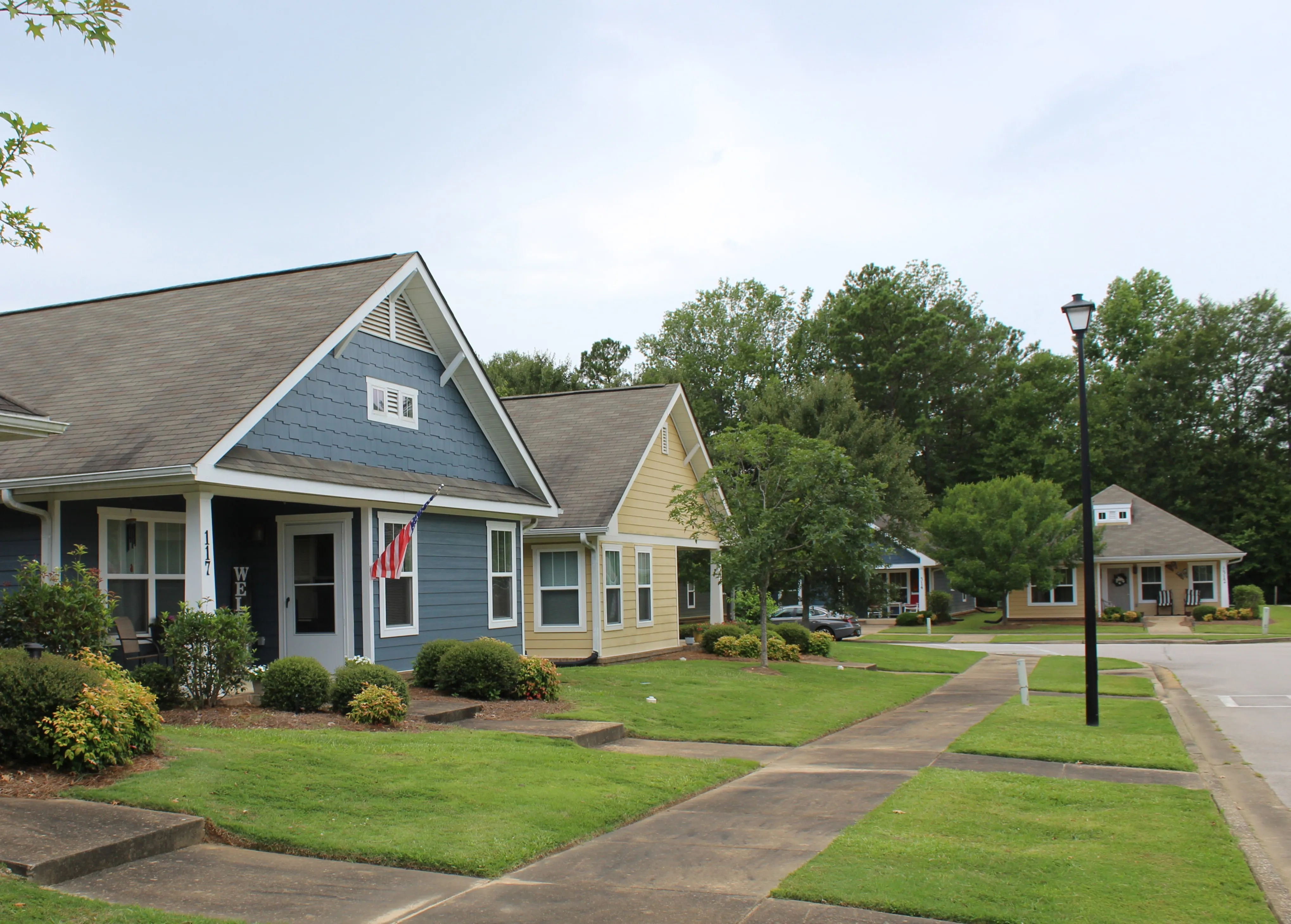 Two-story gray house with white trim, a front porch, and a landscaped front yard on a sunny day.