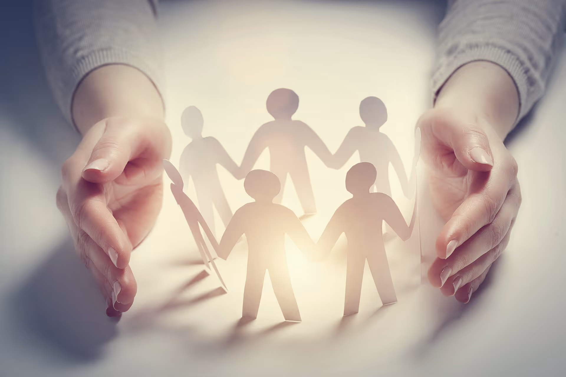 Hände schützen Papierfiguren als Symbol für Team und Zusammenhalt