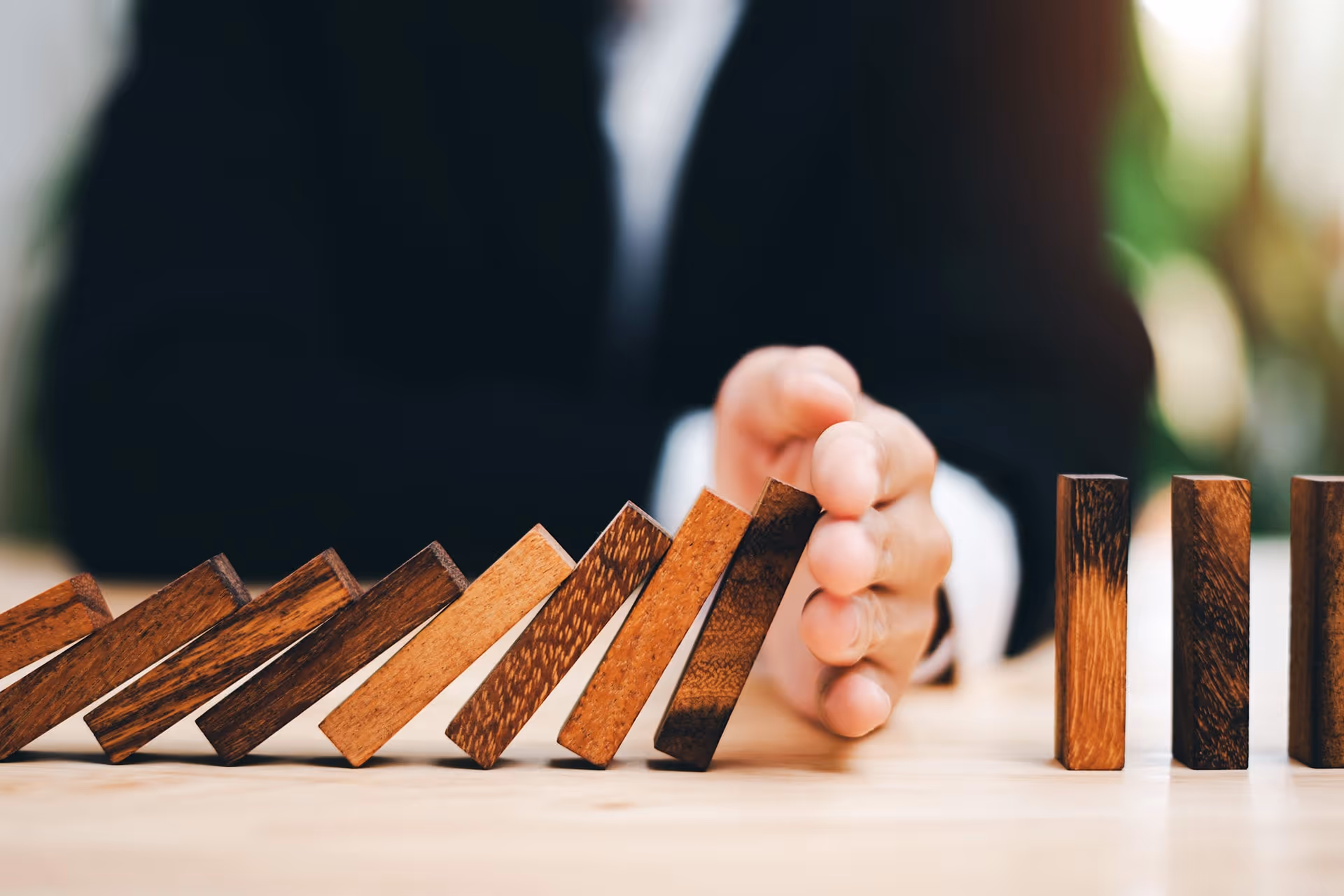 Hand stoppt fallende Domino-Steine als Symbol für Risikokontrolle