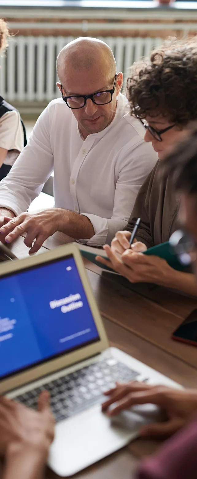 Two men in glasses collaborating over notes and a laptop displaying a discussion outline.