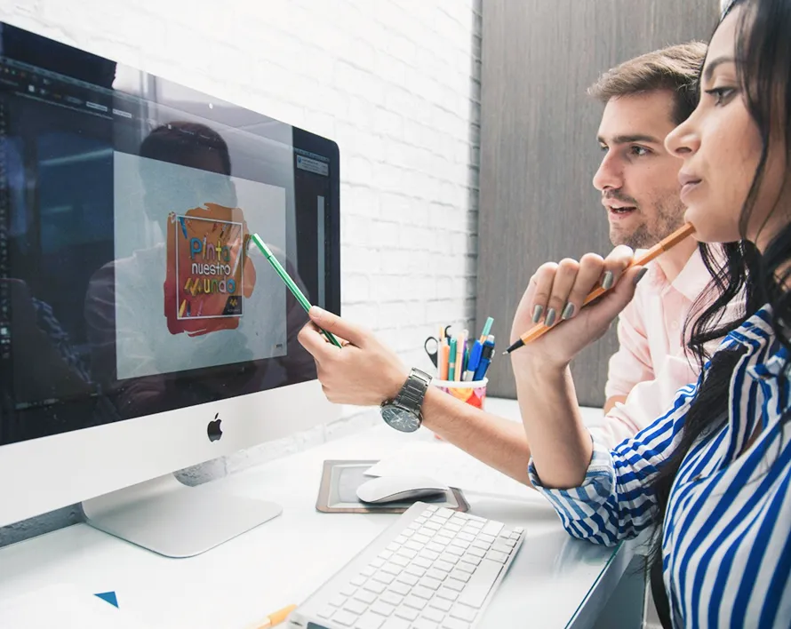 Two people collaborating and pointing at a computer screen displaying colorful text and graphics.