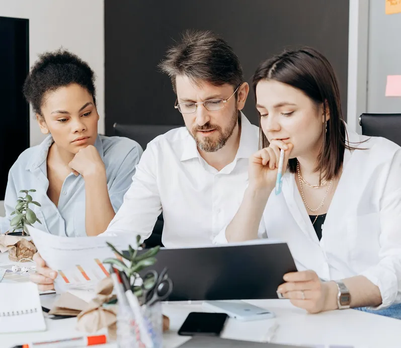 Three coworkers reviewing documents together at a desk in an office setting.