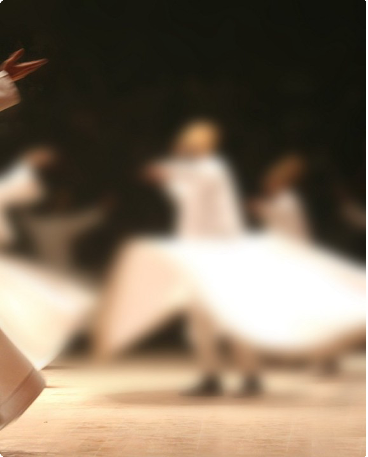 Whirling dancers in long white robes spinning on a wooden floor, captured in soft motion blur.