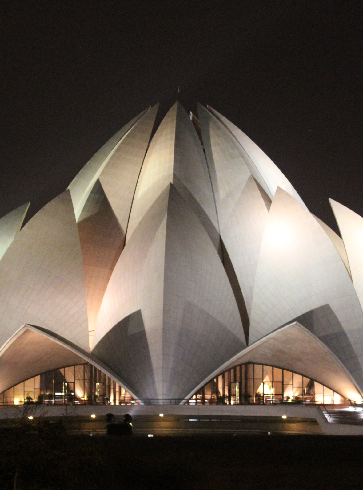 White lotus-shaped building lit up at night against a dark sky, the Báhá’í House of Worship in New Delhi.