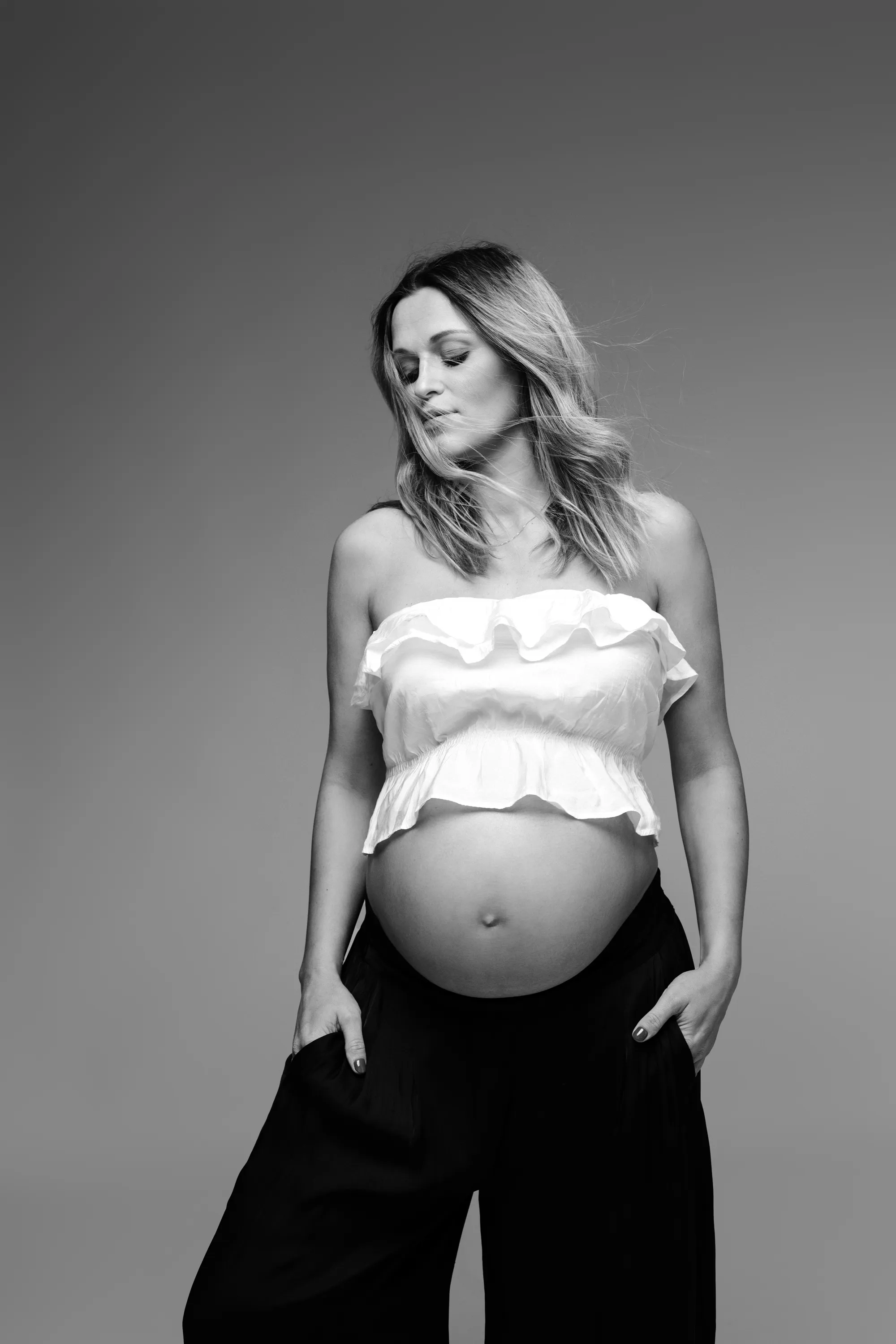Subtelna sesja ciążowa w studio – portret kobiety w białym topie i czarnych spodniach, Wrocław.