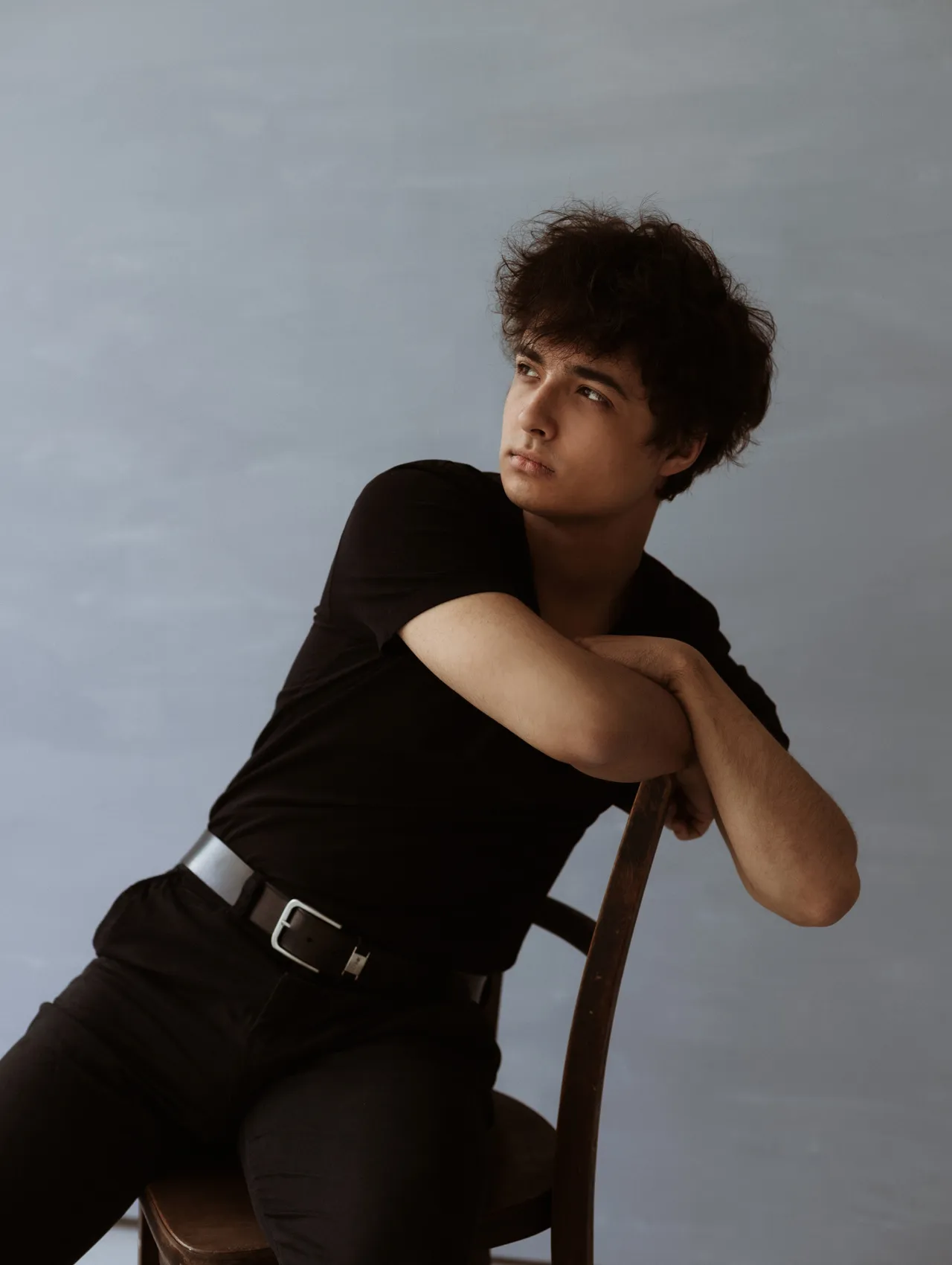 Portret mężczyzny w czarnym ubraniu wykonany w studio fotograficznym w Opolu, siedzącego na drewnianym krześle.