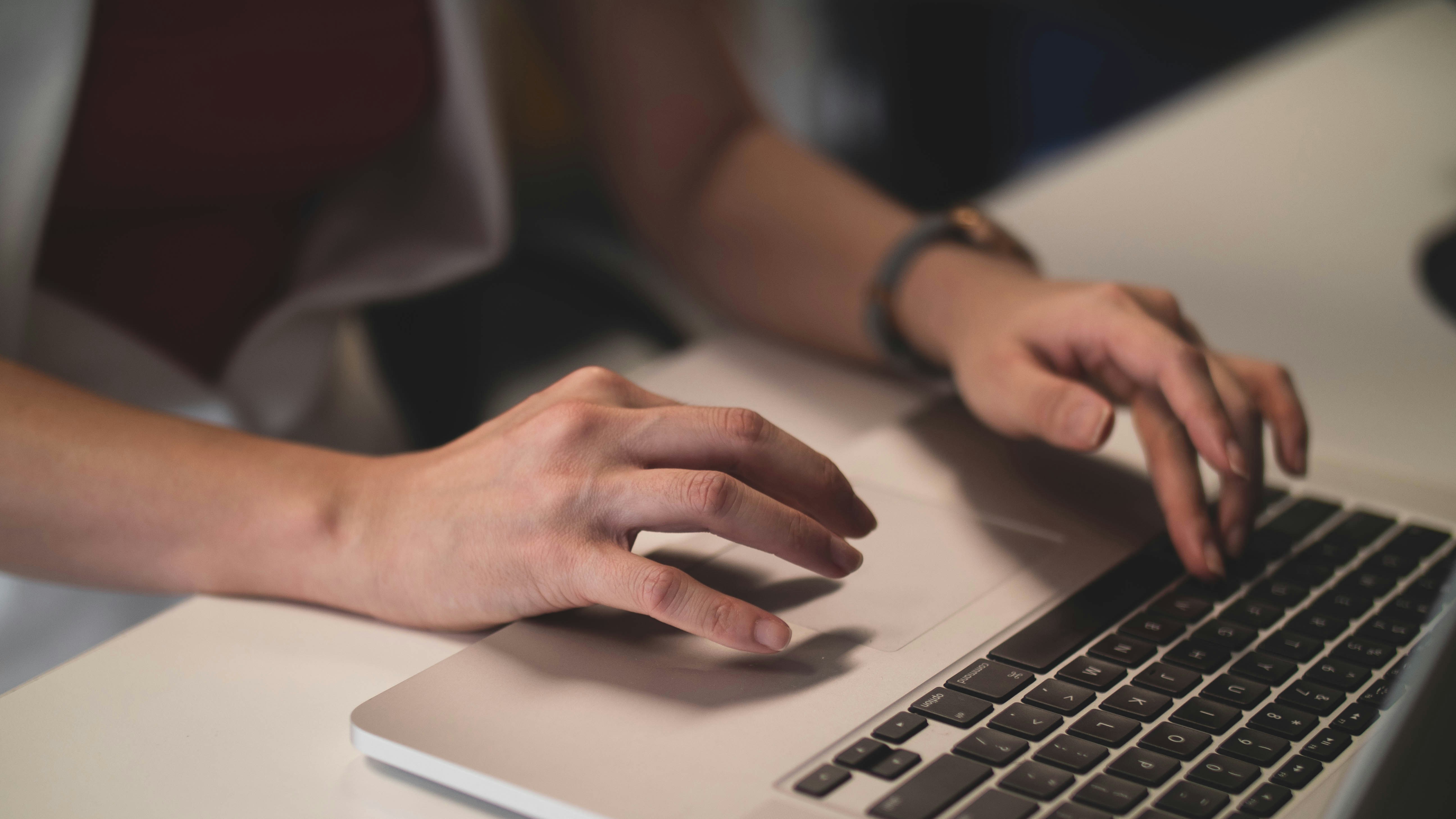 Close-up of hands typing on laptop keyboard with bracelet visible