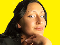 Close-up of a woman with dark hair against a bright yellow background, resting her chin on her hand.