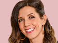 Smiling woman with long brown hair, wearing hoop earrings, against a pink background.