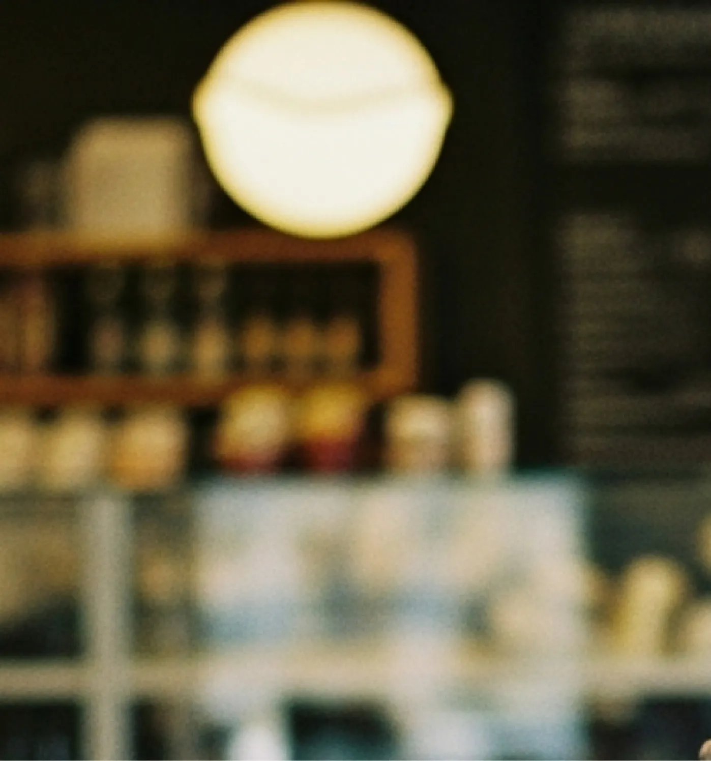 Blurred interior of a café with shelves, bottles, and a large glowing circular light.