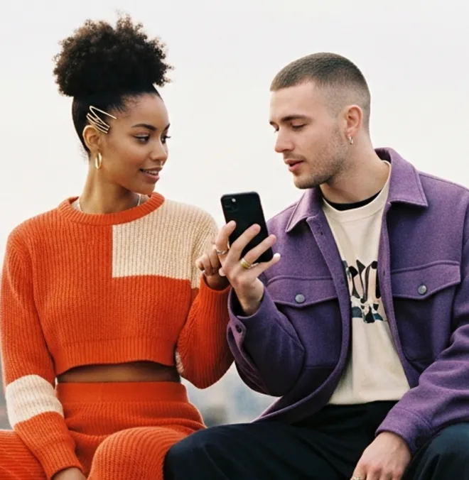 A man and woman sitting next to each other looking at a smartphone together.