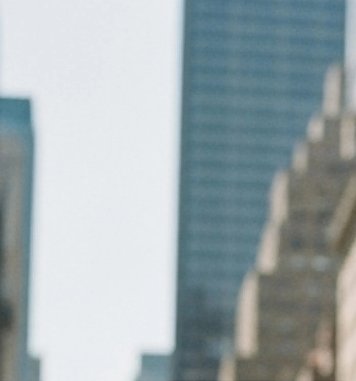 Blurred urban scene with tall buildings and blue sky in the background.