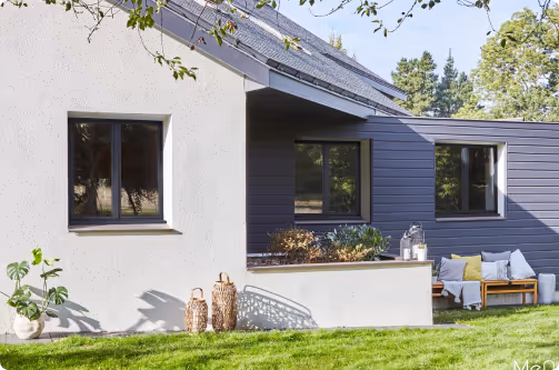 Maison moderne avec façade blanche et grise, terrasse avec mobilier d'extérieur et pelouse verte.