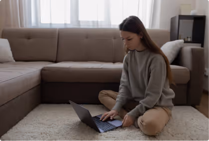 Jeune femme assise par terre dans un salon, travaillant sur un ordinateur portable.