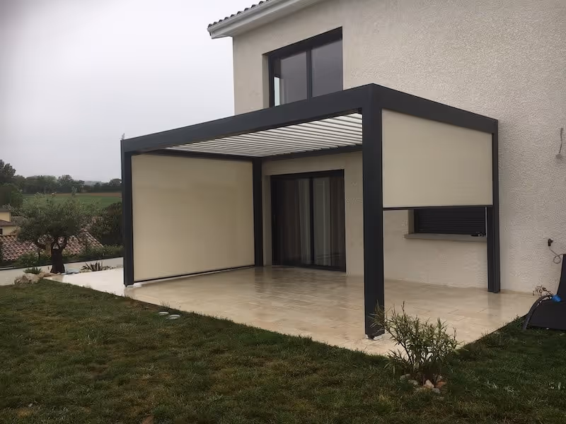 Pergola moderne en métal noir avec panneaux latéraux beiges sur une terrasse carrelée attenante à une maison.