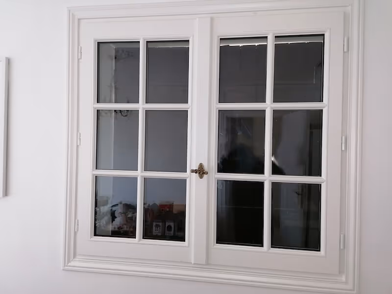 Fenêtre double blanche à six carreaux de chaque côté avec poignée centrale dorée.
