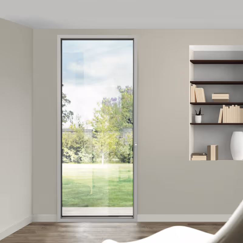 Baie vitrée donnant sur un jardin avec herbe verte et arbres, dans un salon moderne avec étagères intégrées et fauteuil blanc.