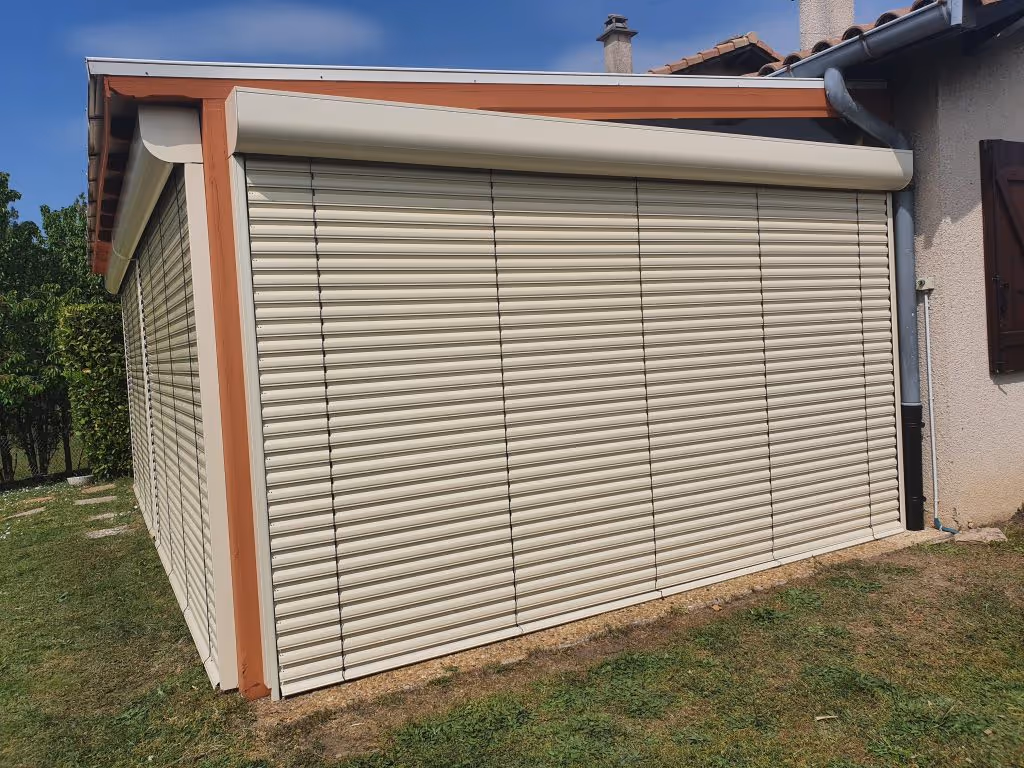Extérieur d'une maison avec des volets roulants en aluminium beige fermés sur une terrasse.