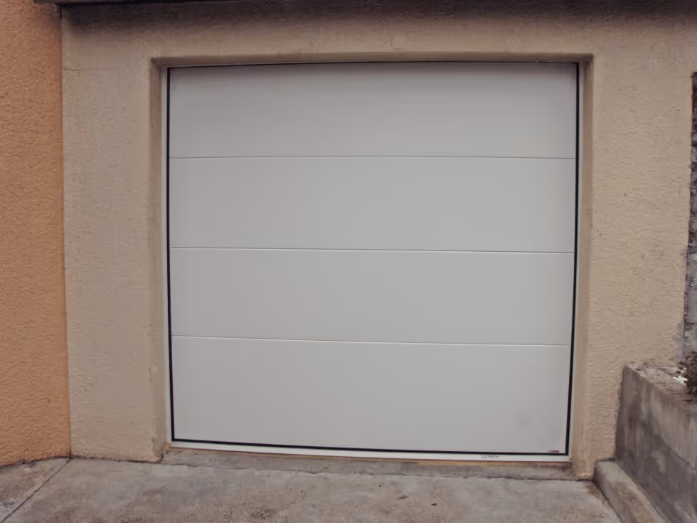 Porte de garage blanche moderne encadrée par un mur en crépi beige.