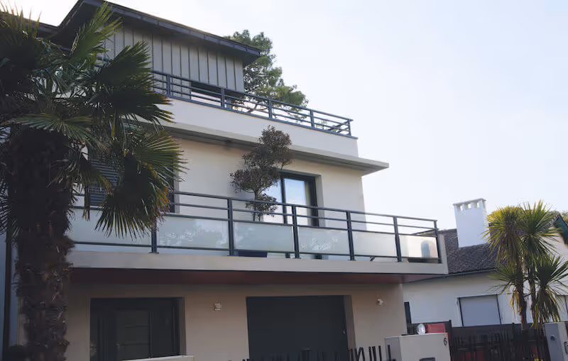 Façade d'une maison moderne à deux étages avec balcon, entourée de palmiers.