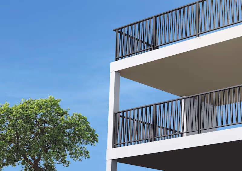 Coin d'un bâtiment moderne avec balcons à rambarde noire contre un ciel bleu et un arbre vert.