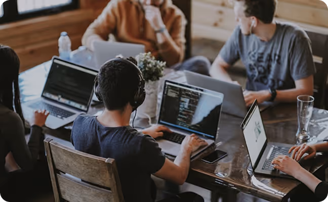 Employés de bureau diversifiés portant des casques, collaborant et travaillant sur des ordinateurs portables dans un bureau moderne à aire ouverte avec des murs en verre et une baie de serveurs.