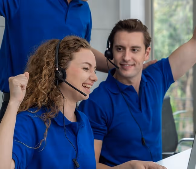 Diverse office workers wearing headsets, collaborating and working on laptops in a modern open-plan office with glass walls and a server rack.