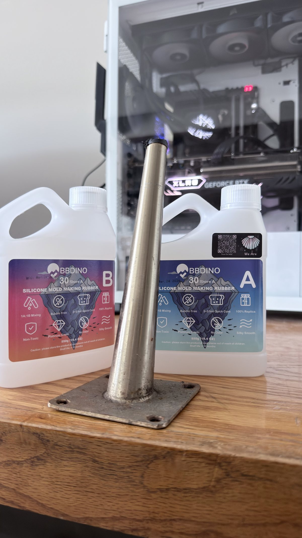 Two bottles of platinum-cure silicone mould rubber on a wooden table beside a salvaged tapered metal furniture leg mounted on a square flange plate.
