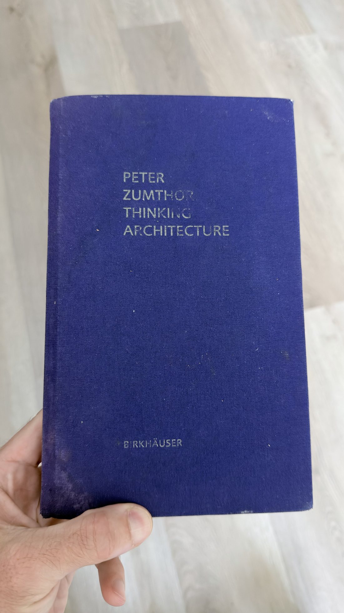 A worn blue cloth hardback of Peter Zumthor's Thinking Architecture held in one hand.