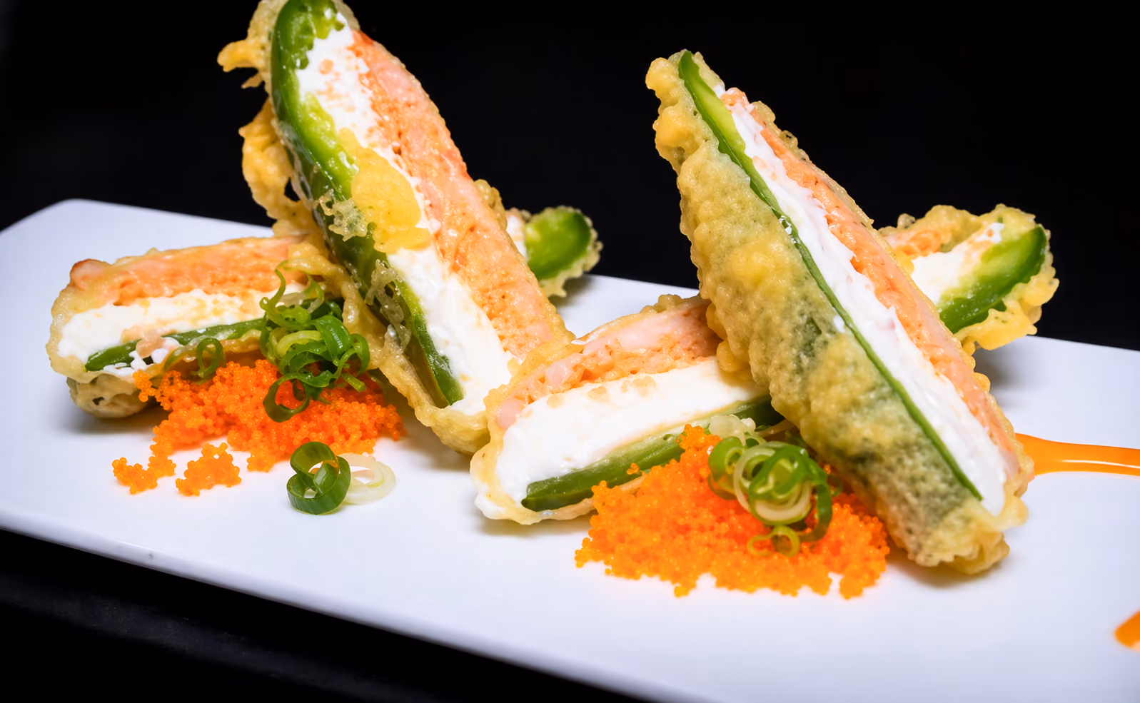 Tempura fried stuffed jalapeños with cream cheese, salmon, and garnished with green onions and orange fish roe.