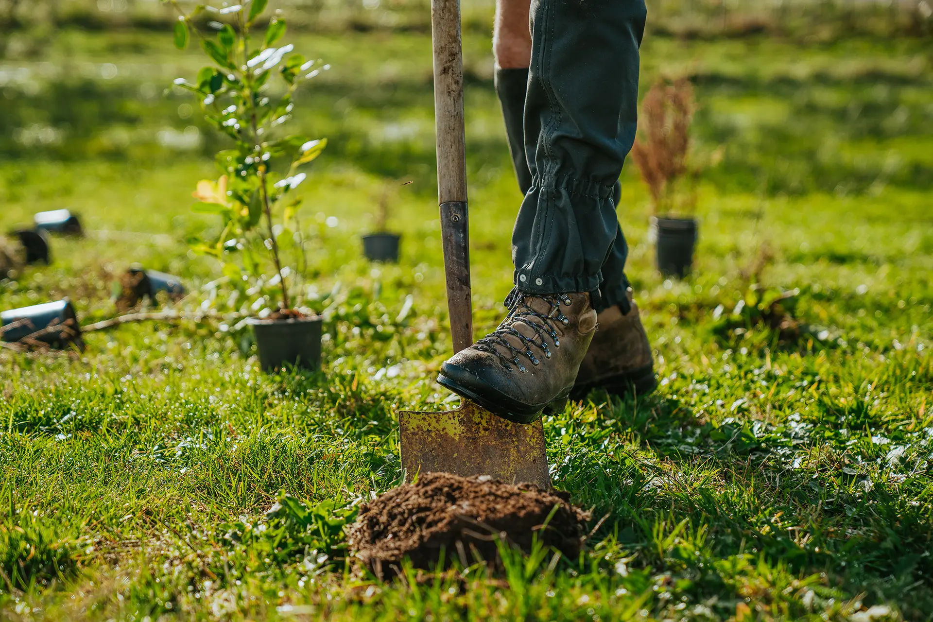 Two men talking near a red Kubota tractor in a field with trees and another person in an orange safety jacket in the background.