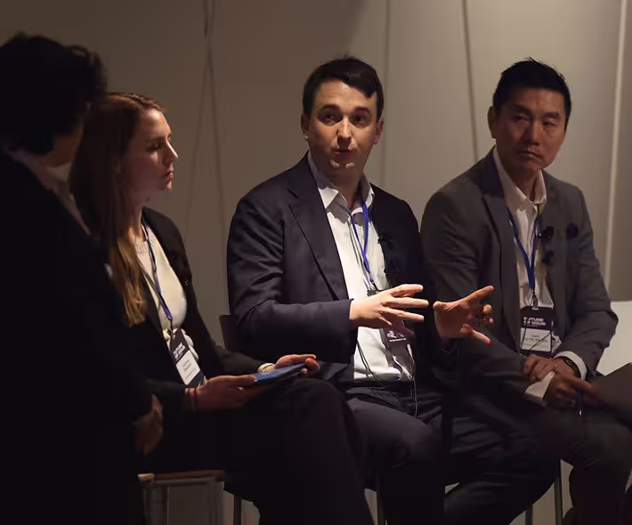 Four professionals seated and engaged in a panel discussion, with one man gesturing while speaking.