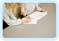 Two people collaborating over documents on a table, one pointing at a paper with a pen.