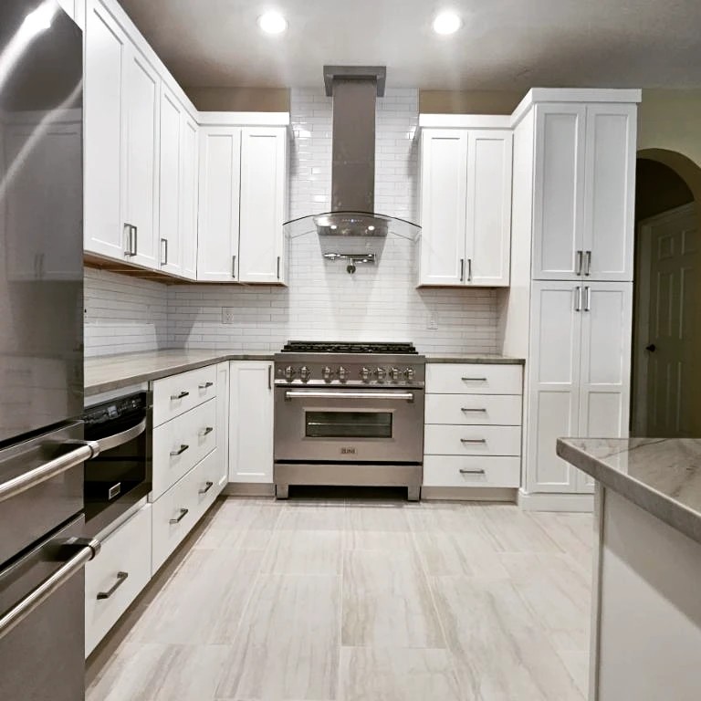 Modern kitchen by Gonzo Interiors featuring custom white cabinetry, a stylish curved glass range hood, and a clean white subway tile backsplash