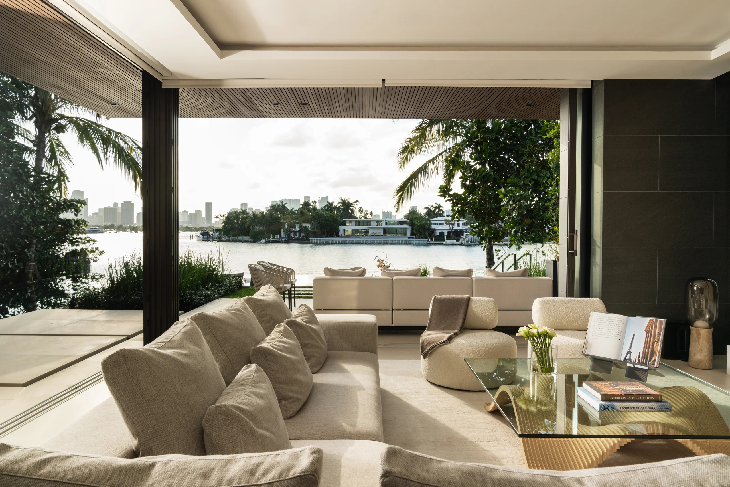 Living room opening onto a waterfront terrace with palm trees and Miami skyline views, Miami's Rive Gauche project by Dunagan Design.