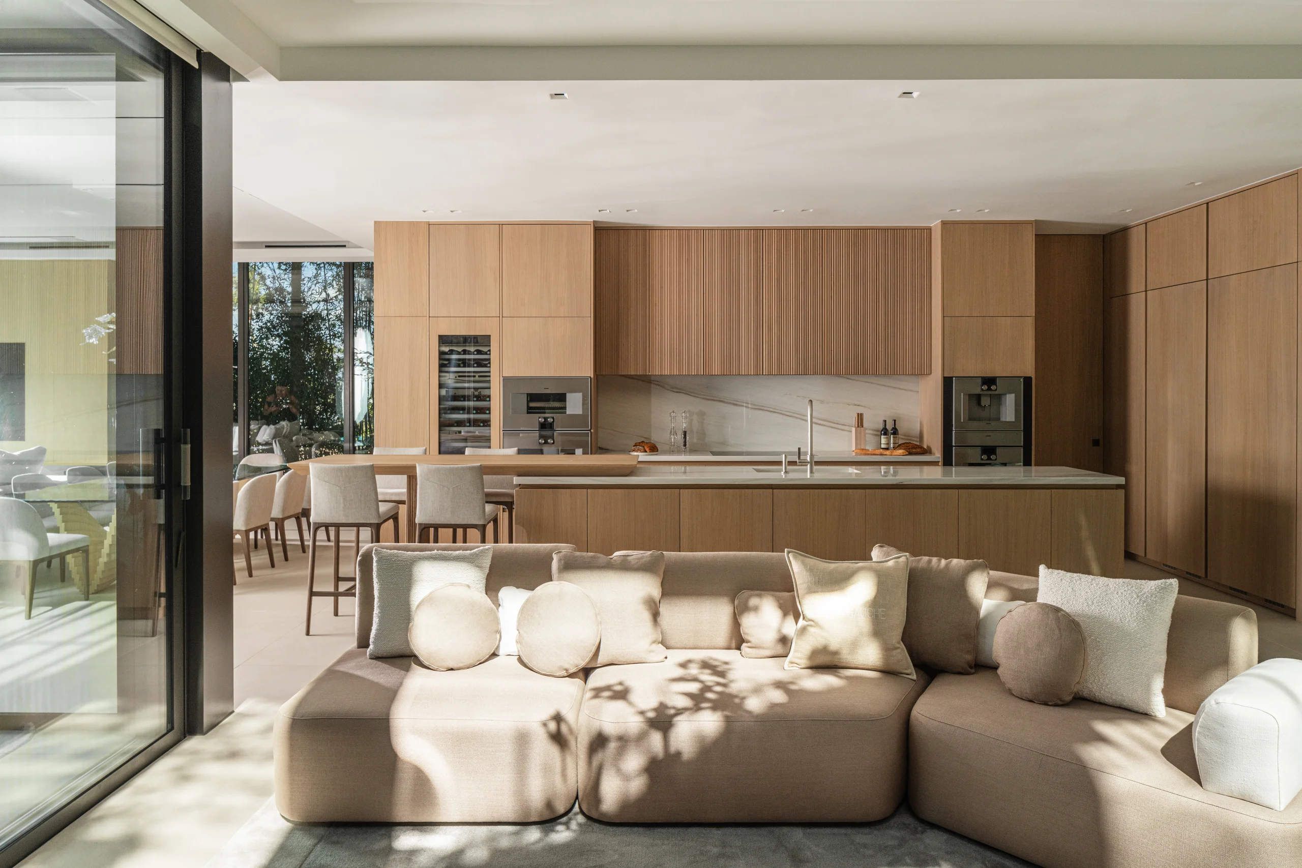 Open kitchen with white oak cabinetry flowing into the living room's sectional seating, Miami's Rive Gauche project by Dunagan Design.