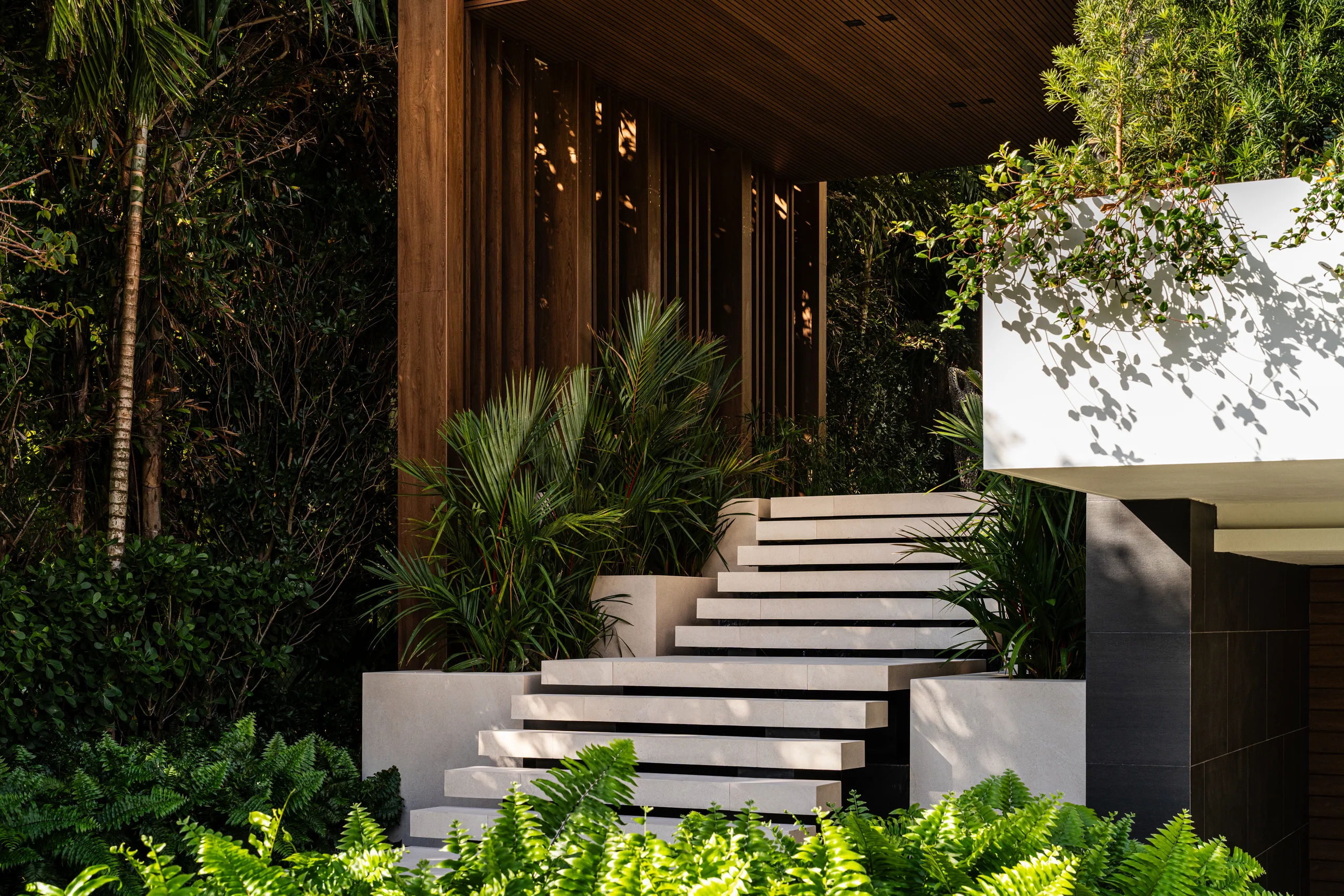 Floating stone entry staircase set against a wood-slat wall and lush tropical planting, Miami's Rive Gauche project by Dunagan Design.