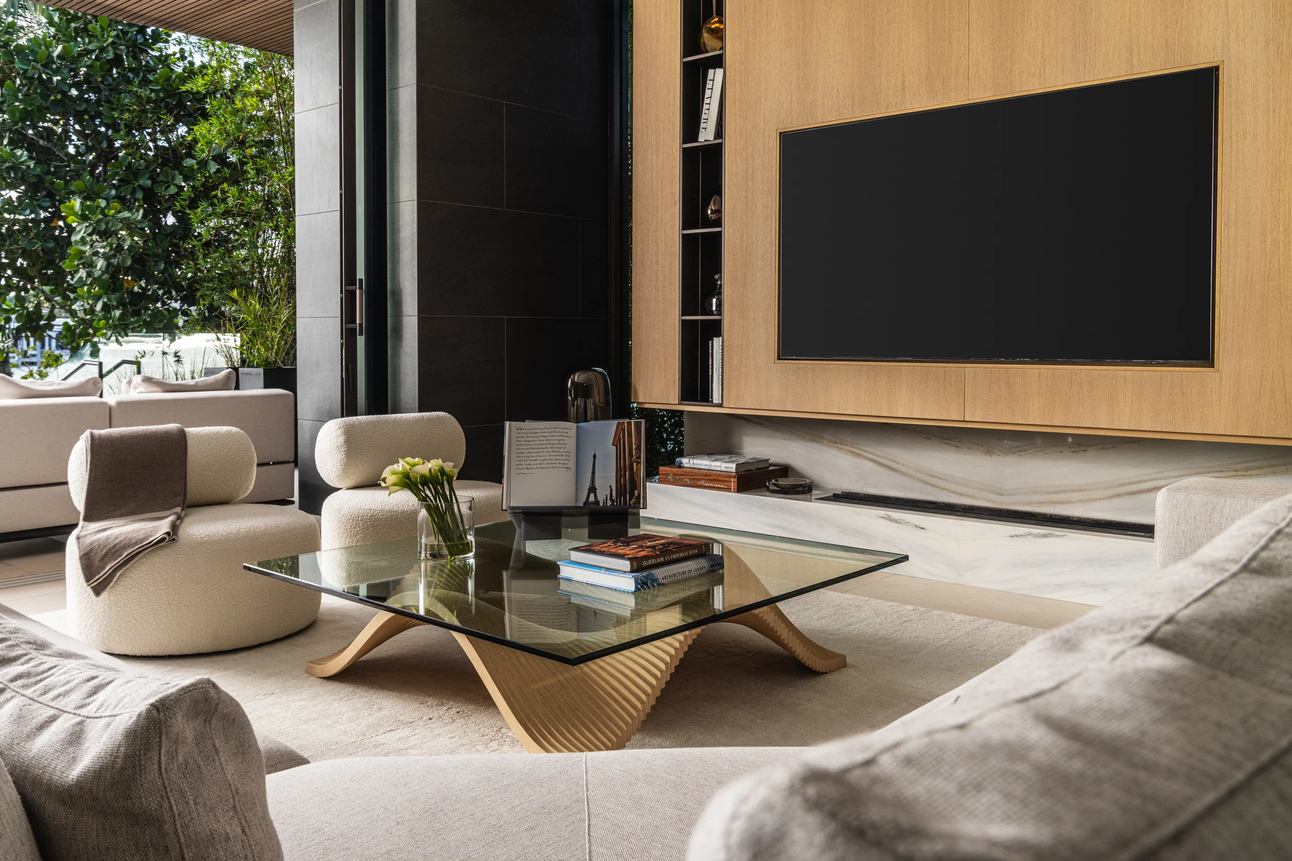 Living room with cream boucle chairs and a sculptural coffee table, opening onto a landscaped terrace, Miami's Rive Gauche project by Dunagan Design.