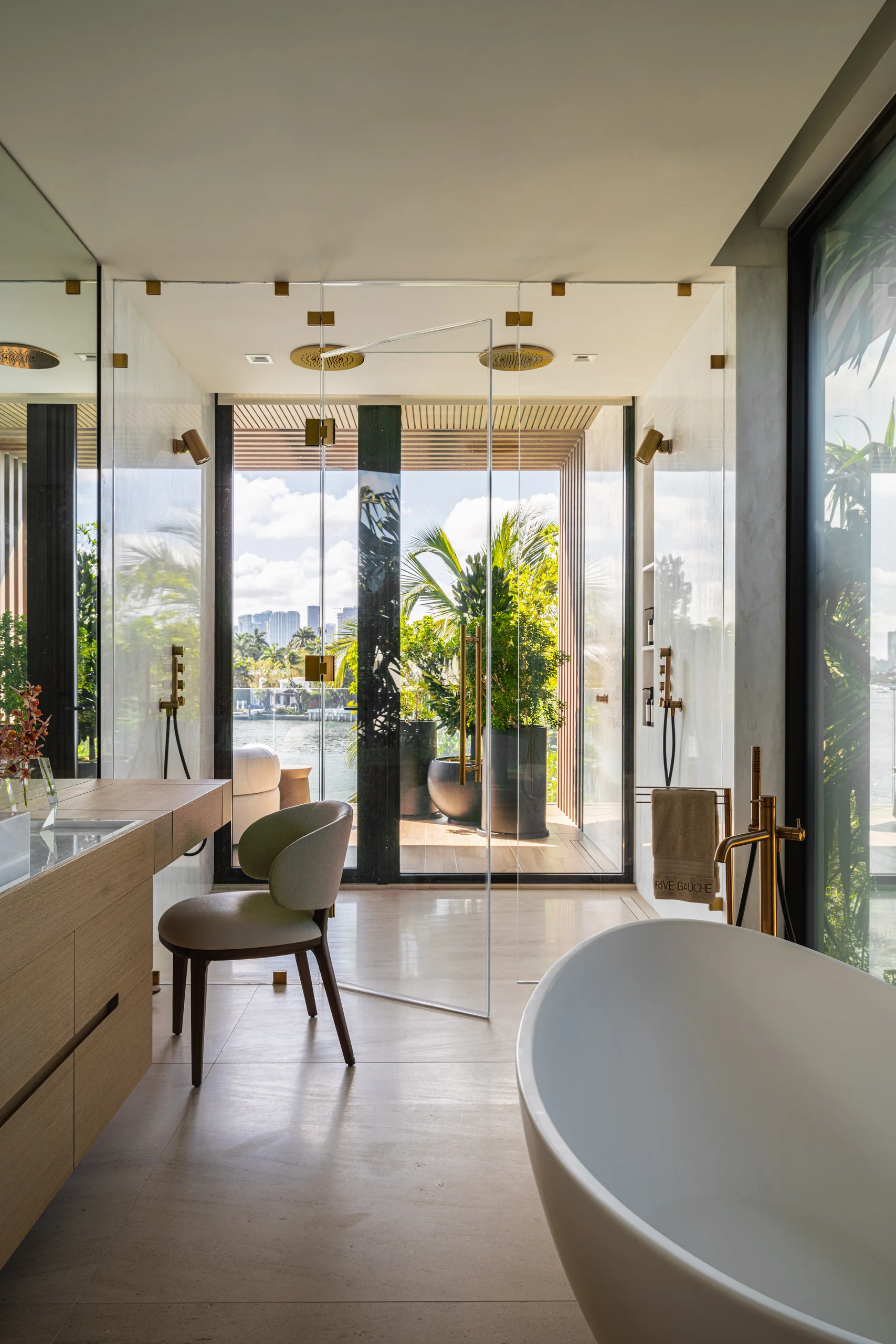 Primary bathroom with a freestanding soaking tub, glass rain shower, and white oak vanity overlooking the city, Miami's Rive Gauche project by Dunagan Design.