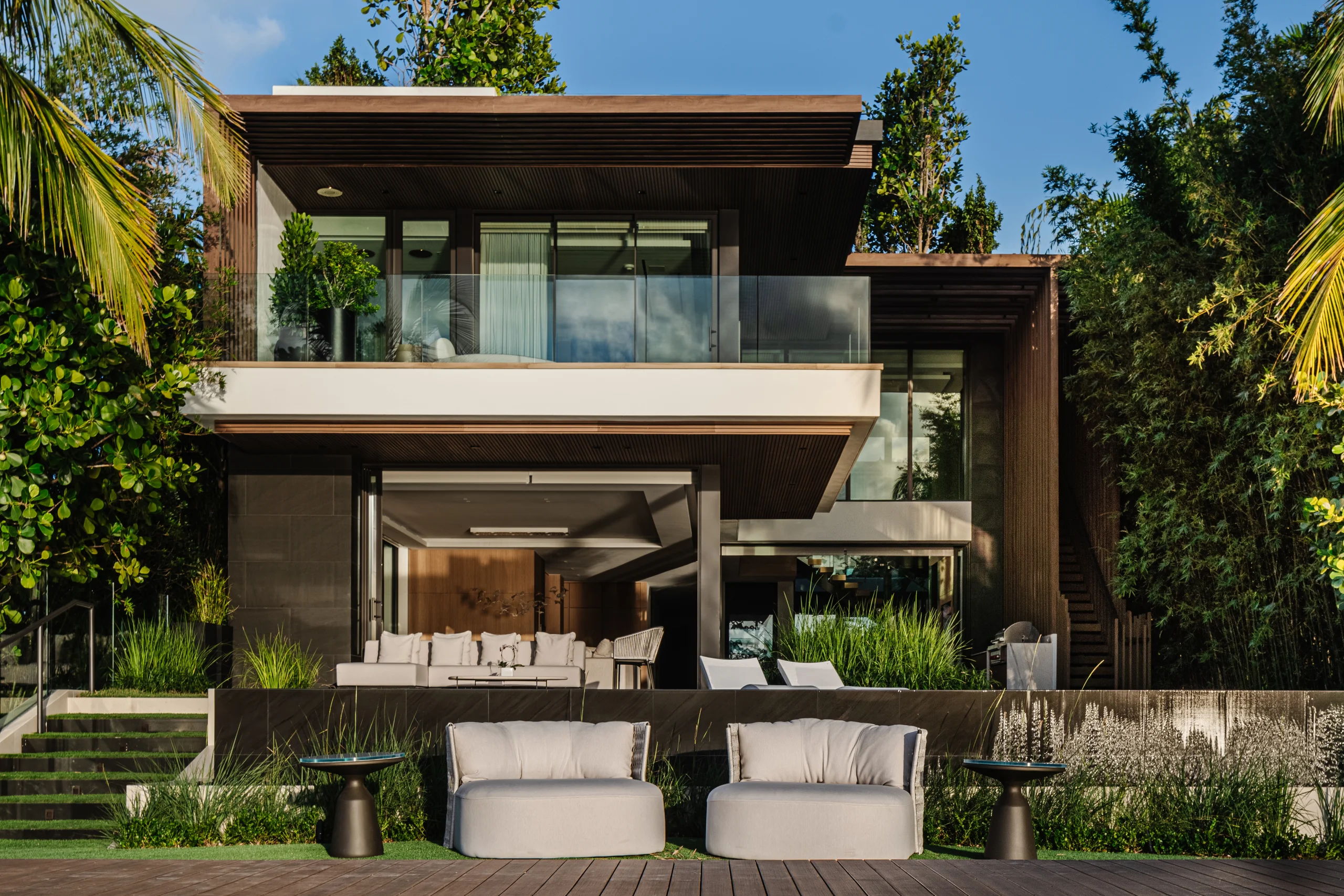 Rear exterior of a two-story wood-clad residence with a wraparound balcony and outdoor lounge seating, Miami's Rive Gauche project by Dunagan Design.