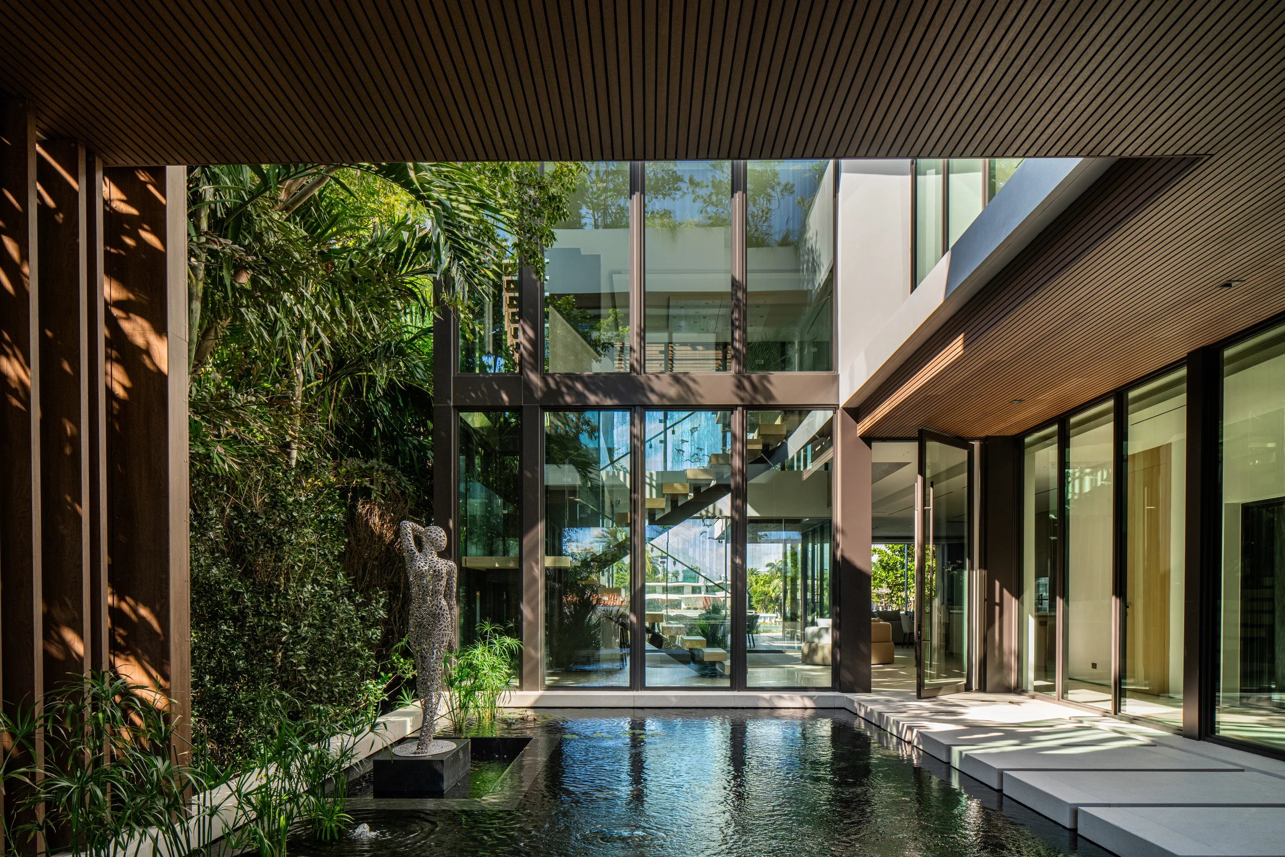 Courtyard reflecting pool and wire-mesh sculpture framed by the home's multi-story glass facade, Miami's Rive Gauche project by Dunagan Design.