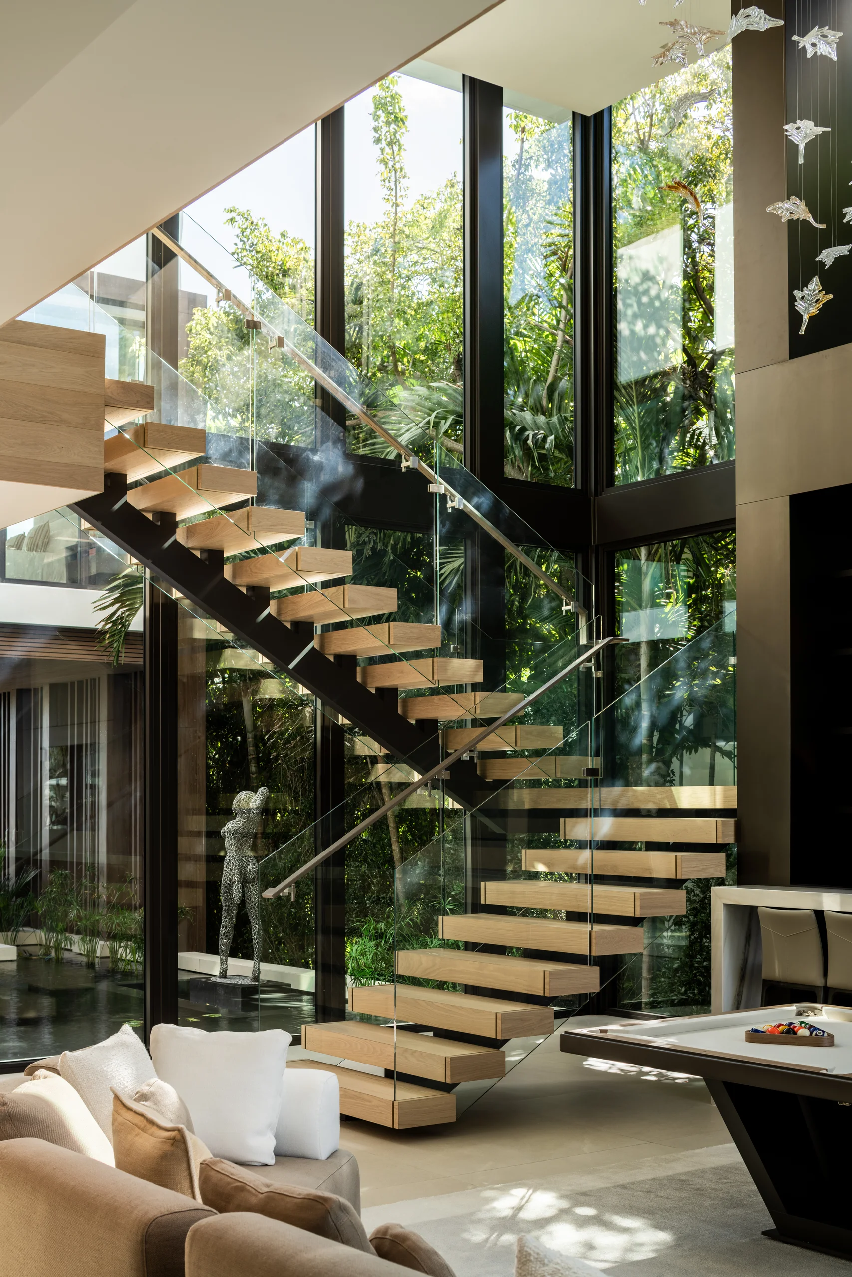 Floating wood-and-glass staircase beneath a double-height window wall overlooking the courtyard and game room, Miami's Rive Gauche project by Dunagan Design.