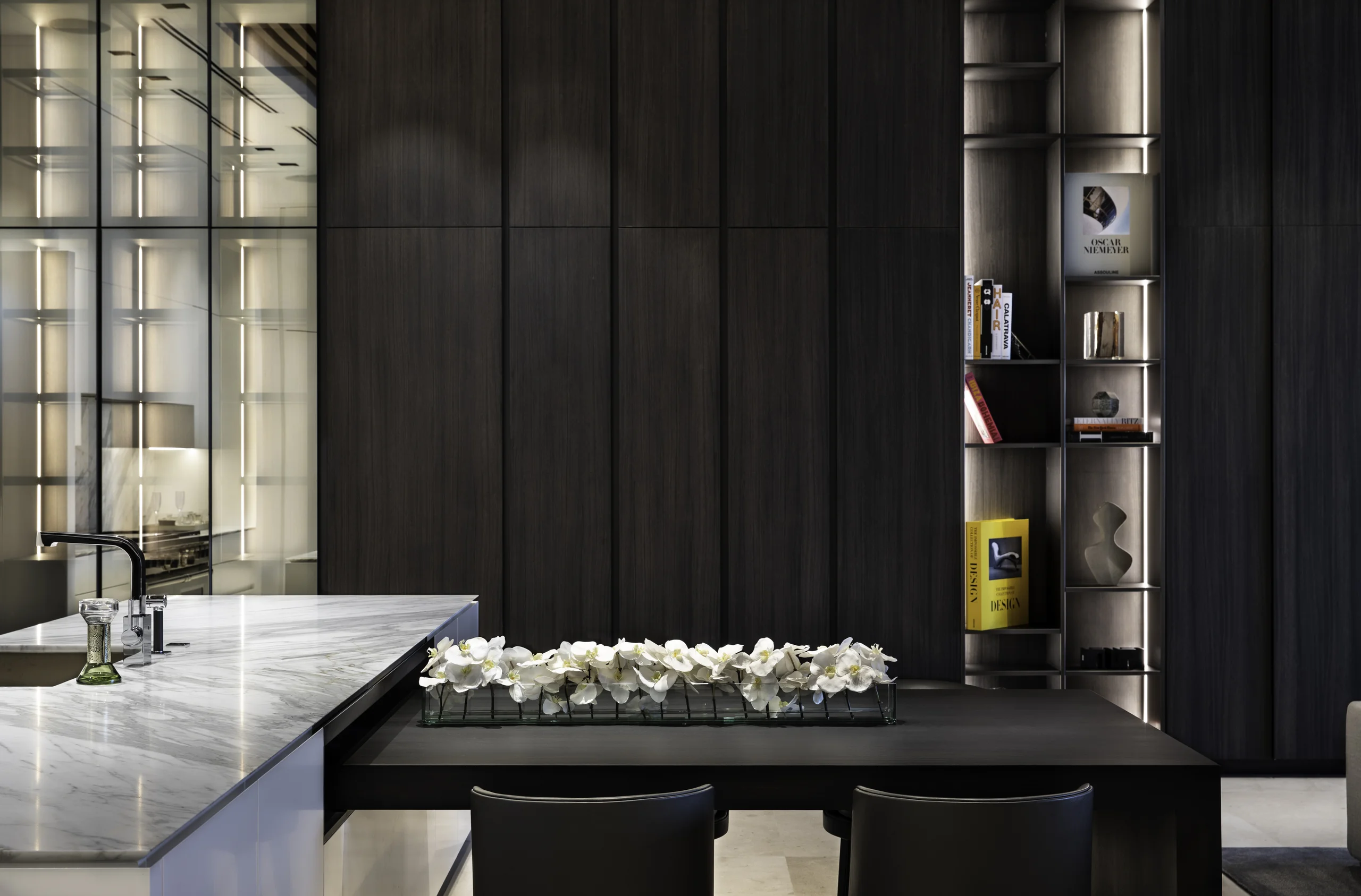 Kitchen island and dining nook with dark wood paneling and a lit display shelf styled with design books and objects, Star Island Waterfront project by Dunagan Design.