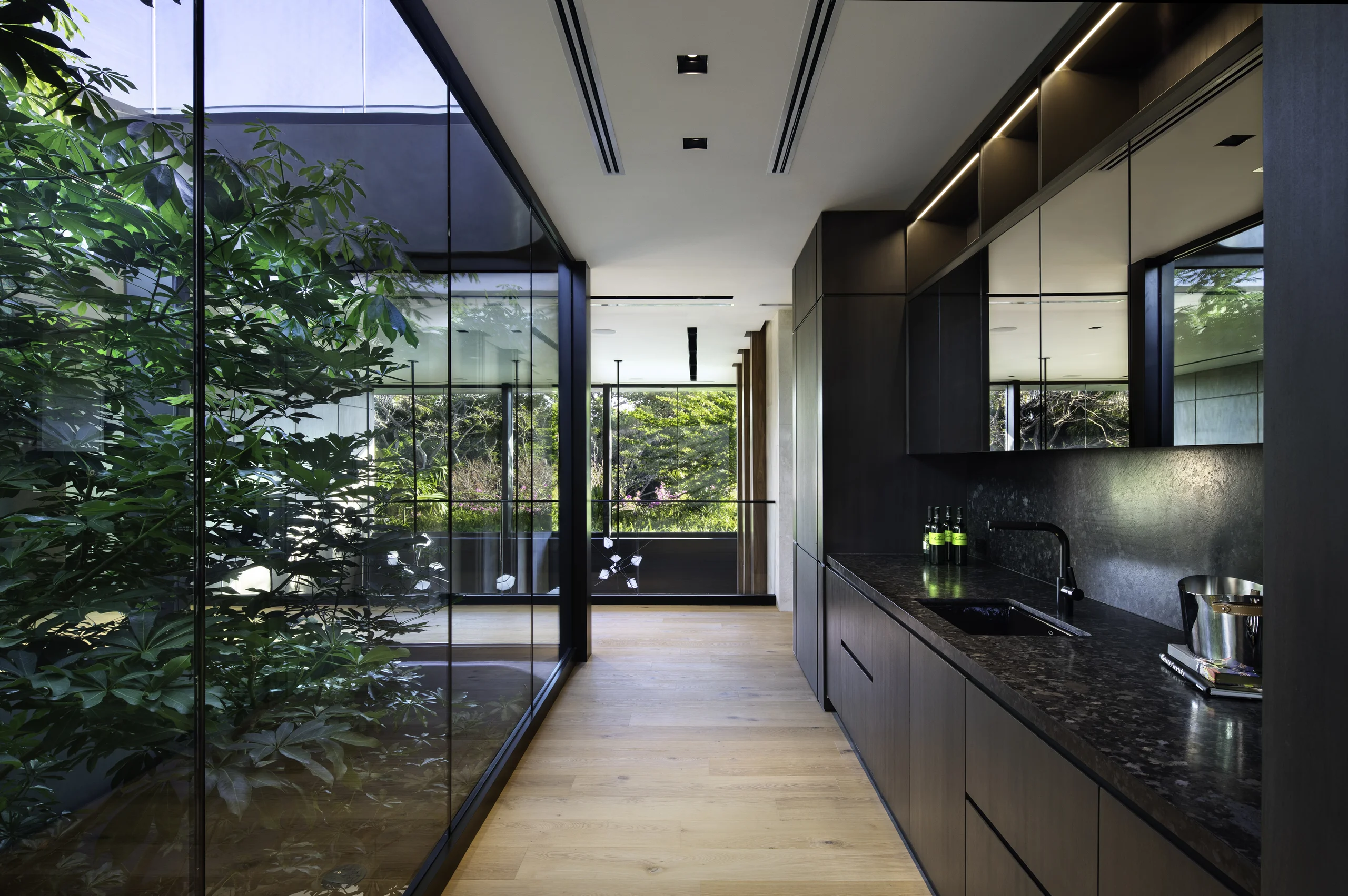 Butler's pantry corridor with a dark stone counter and a mirrored glass wall reflecting the interior garden, Star Island Waterfront project by Dunagan Design.