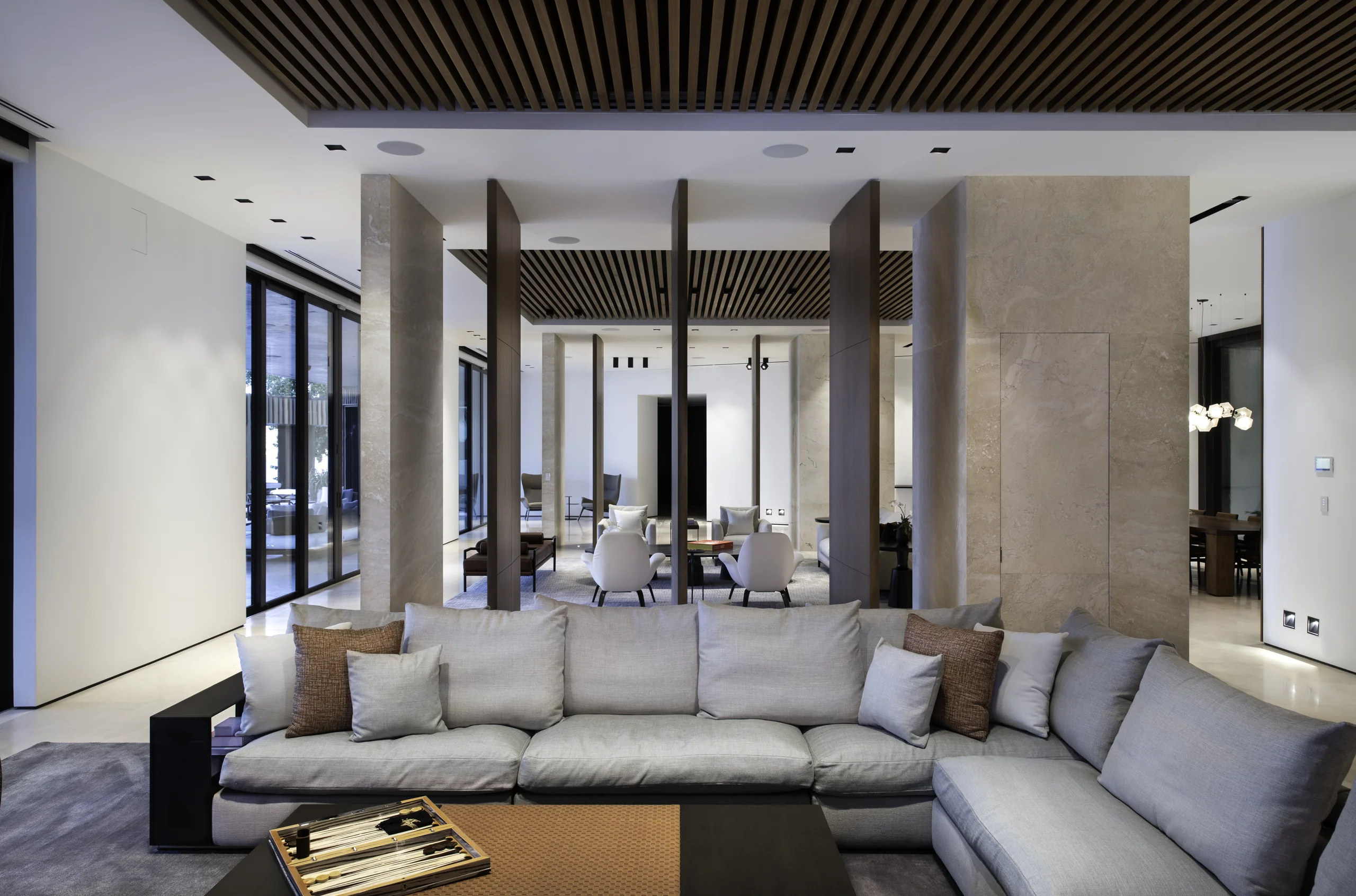 Great room framed by travertine columns, with gray sectional seating and sightlines through to the dining and seating areas, Star Island Waterfront project by Dunagan Design.
