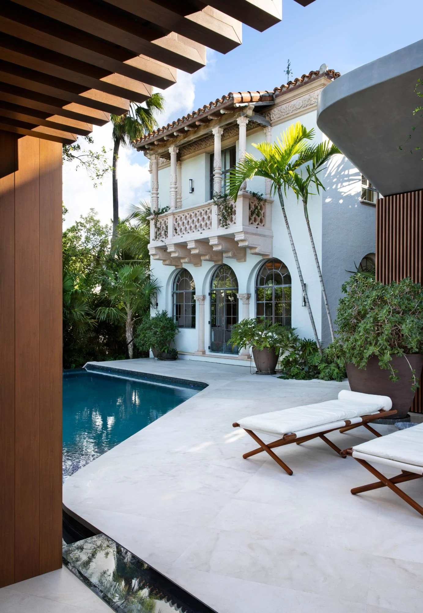 Rear exterior with an ornate cast-stone balcony, arched windows, and a barrel tile roof overlooking the pool and palm-lined terrace, Star Island Waterfront project by Dunagan Design.