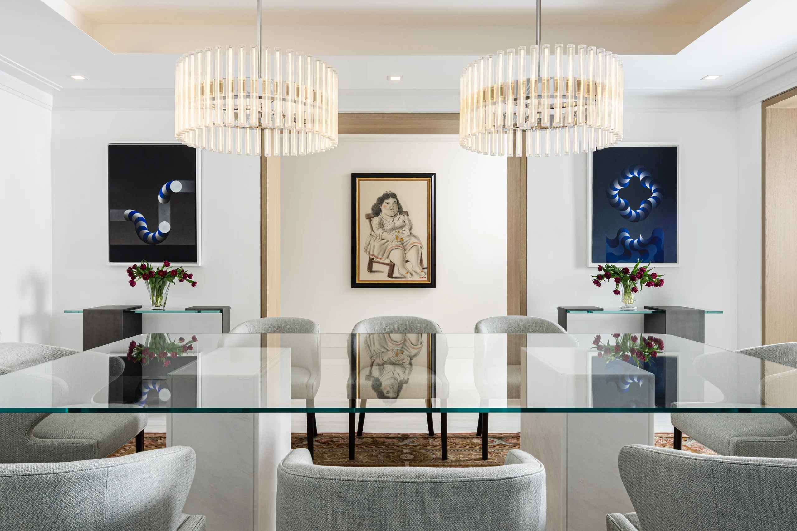 Dining room with a glass-top table, dual crystal chandeliers, and a curated collection of figurative and geometric artwork, Coco Plum Revival project by Dunagan Design.