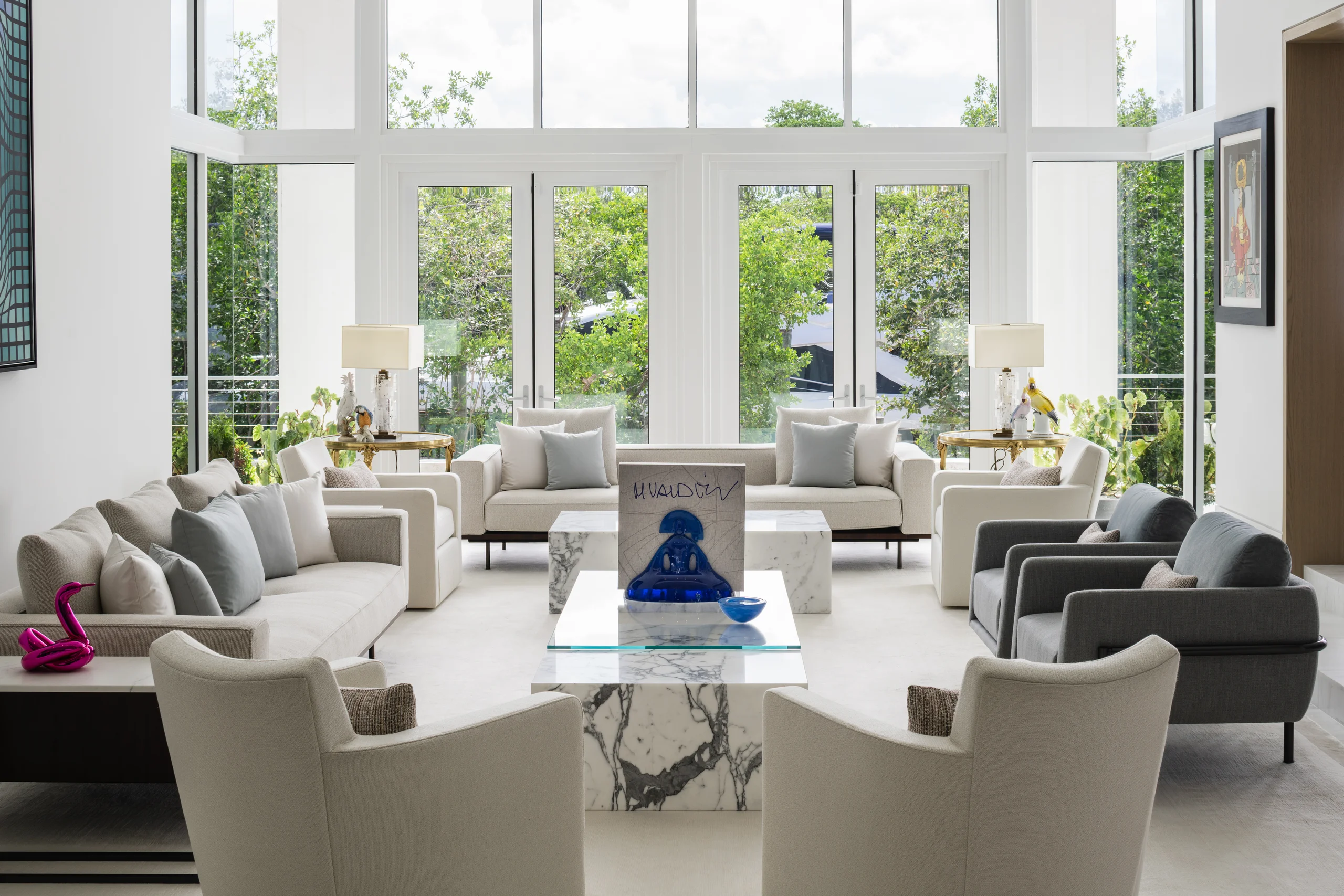 Living room with double-height windows, neutral upholstered seating, and a curated art and sculpture collection, Coco Plum Revival project by Dunagan Design.