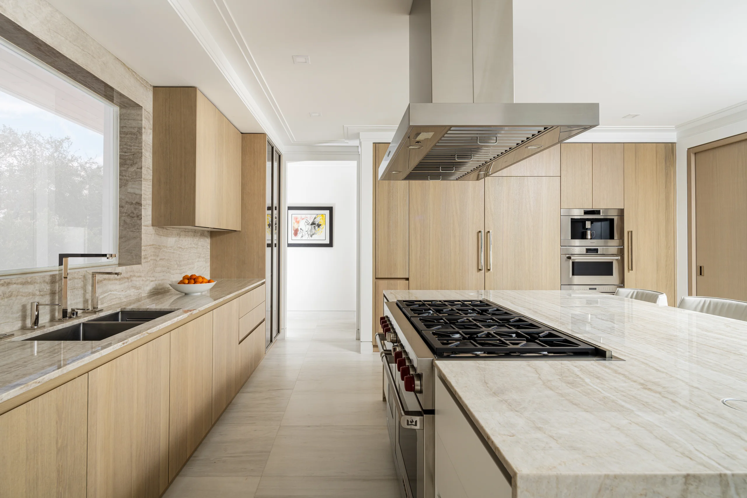 Kitchen with light oak cabinetry, a stone waterfall island, and a professional range with stainless hood, Coco Plum Revival project by Dunagan Design.