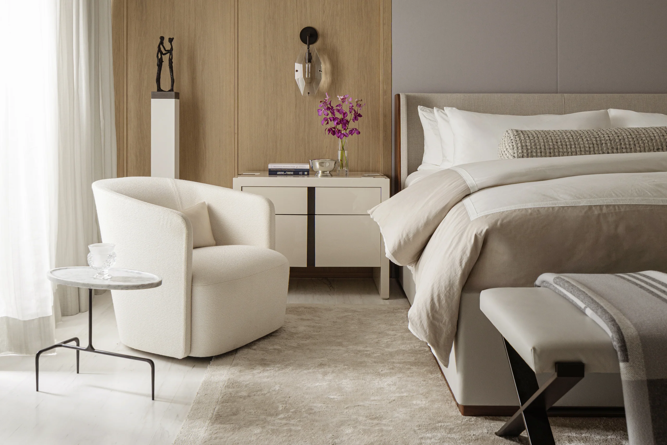 Primary bedroom with a tailored upholstered bed, swivel chair, and bronze figurative sculpture, Coco Plum Revival project by Dunagan Design.